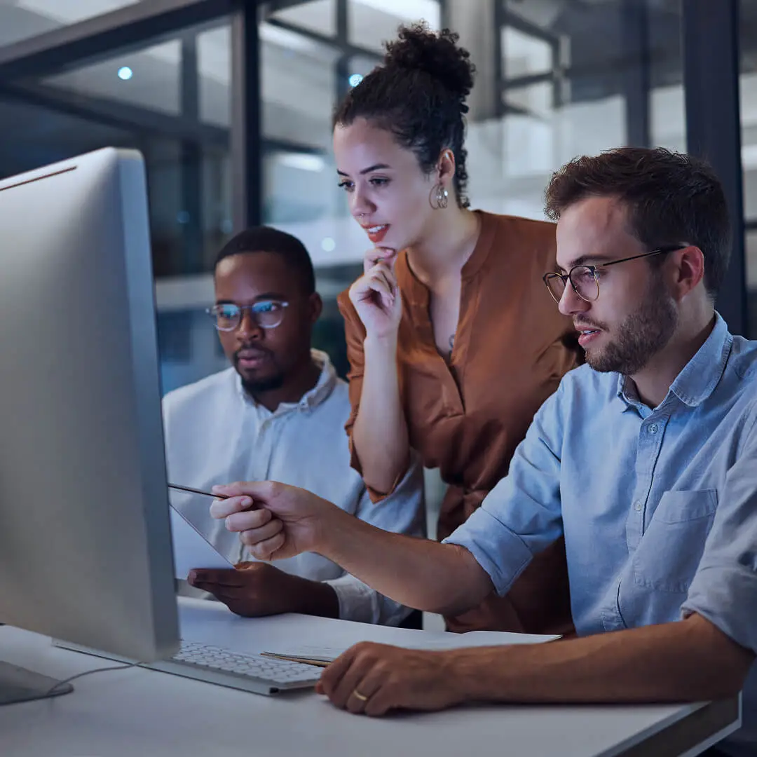 Design team reviewing a website on a desktop computer, with one person pointing at the screen during a collaborative design discussion.