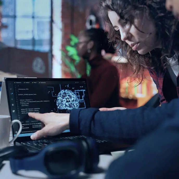 A close-up of two coworkers reviewing code on a laptop showing an AI brain diagram, representing teamwork and human expertise in artificial intelligence.