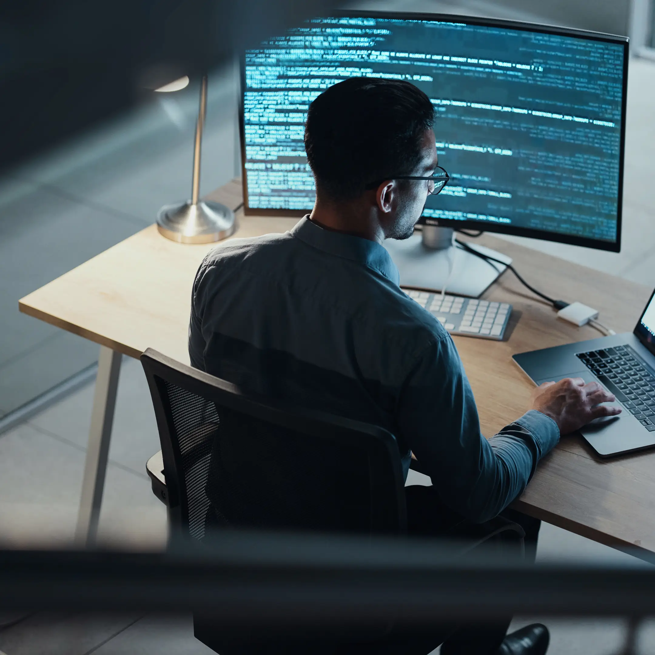 Developer working at a desk with code displayed across a large monitor.