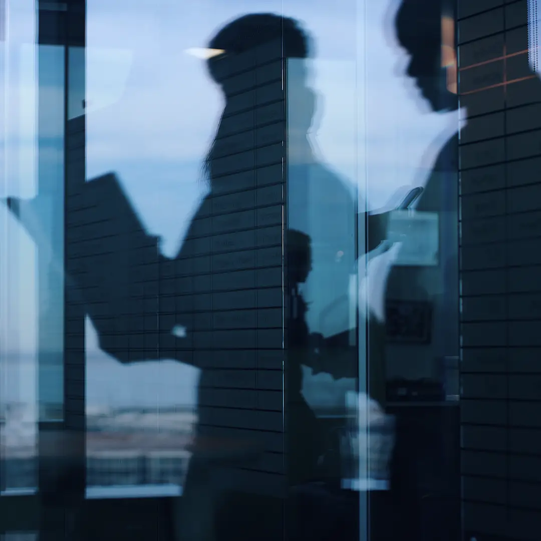 Silhouettes of business professionals meeting behind a glass office wall.