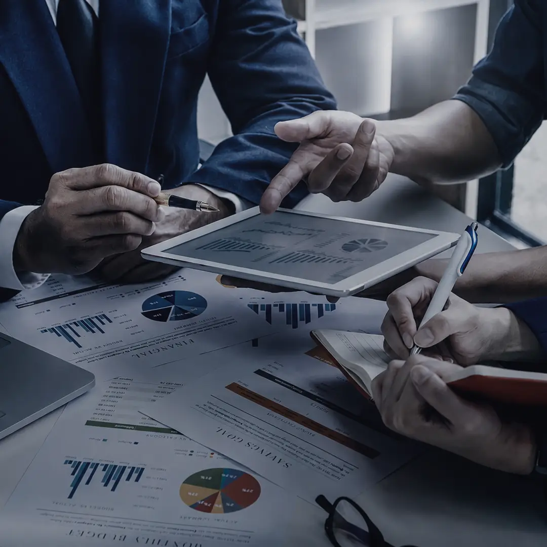 Business professionals reviewing analytics charts and graphs on a tablet and printed reports during a meeting.