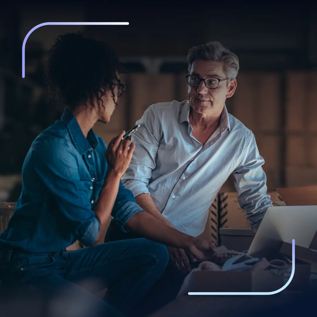 Two professionals reviewing a laptop beside shipping boxes in an ecommerce setting.