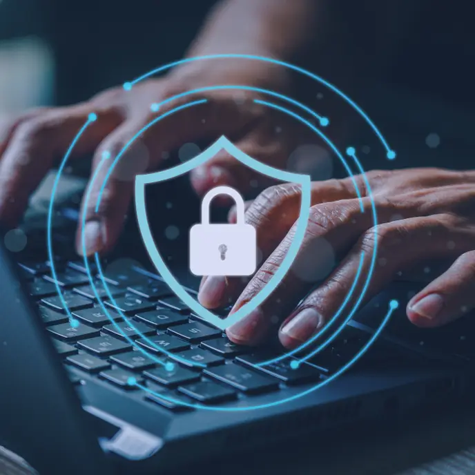 A close-up of hands typing on a laptop keyboard, with a glowing digital shield and padlock icon overlaid to represent cybersecurity and data protection.