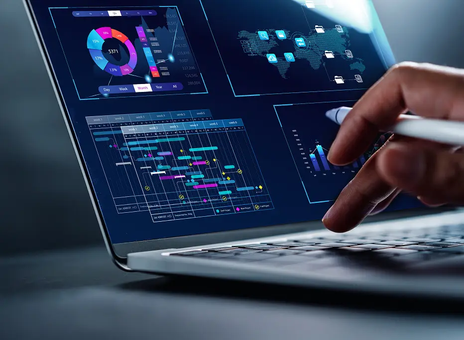A close-up of a laptop screen displaying colorful data dashboards, charts, and a project timeline, while a person uses a stylus to interact with the interface.