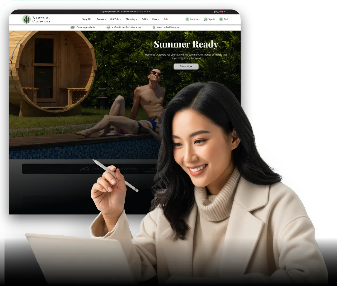 Smiling woman holding a stylus while working on a laptop, with a large tablet screen behind her displaying an outdoor product website featuring a man lounging by a backyard pool next to a wooden sauna.