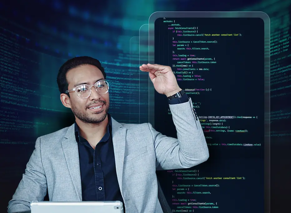 A person wearing glasses and a light gray blazer gestures with one hand while sitting in front of a tablet. Behind them is a large digital screen displaying lines of code with a blue-toned tech background.