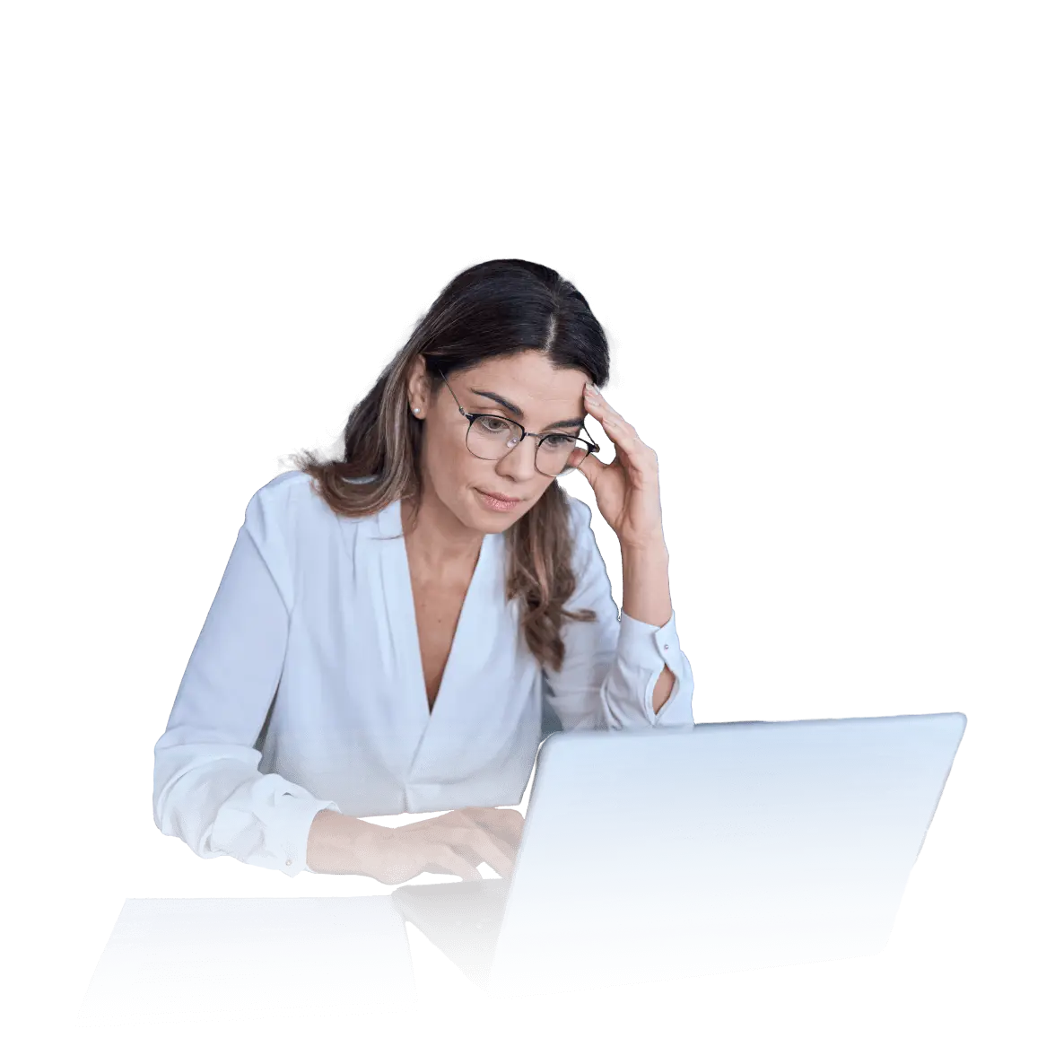 A woman with long brown hair and glasses wearing a white blouse sits at a desk, looking concerned as she works on a laptop, with a paper and pen in front of her.