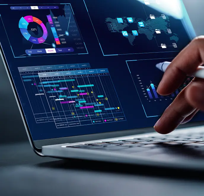 <p>A close-up of a laptop screen displaying multiple digital dashboards, including colorful charts, graphs, and a Gantt-style project timeline. A hand holding a stylus is interacting with the screen, suggesting data analysis or project management work.</p>