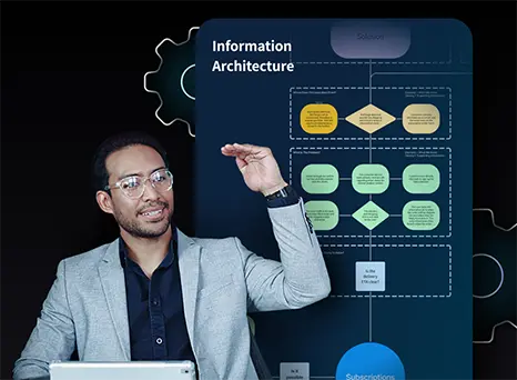 A man wearing glasses and a light gray blazer gestures with his hand while sitting in front of a tablet. Behind him is a large information architecture diagram with flowchart elements in various colors, representing data or system structure.