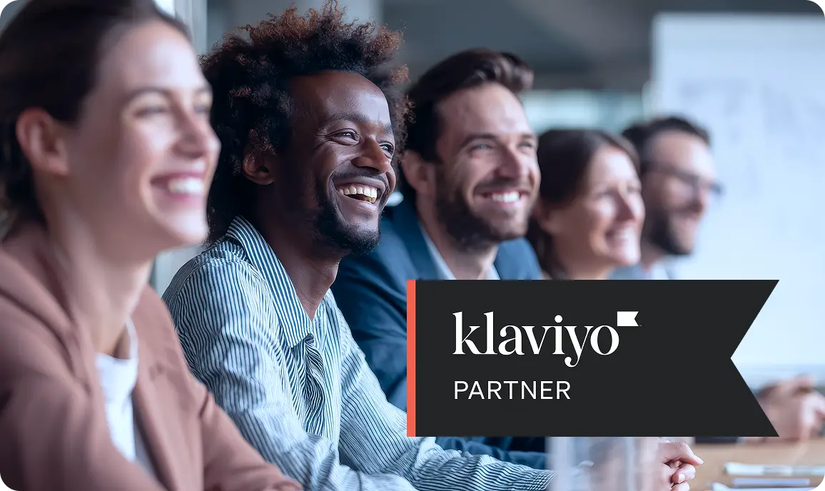 <p>A group of smiling business professionals seated in a meeting room, looking engaged and attentive, with a banner on the right reading &ldquo;klaviyo Partner,&rdquo; representing a collaborative, professional partnership or training session.</p>
