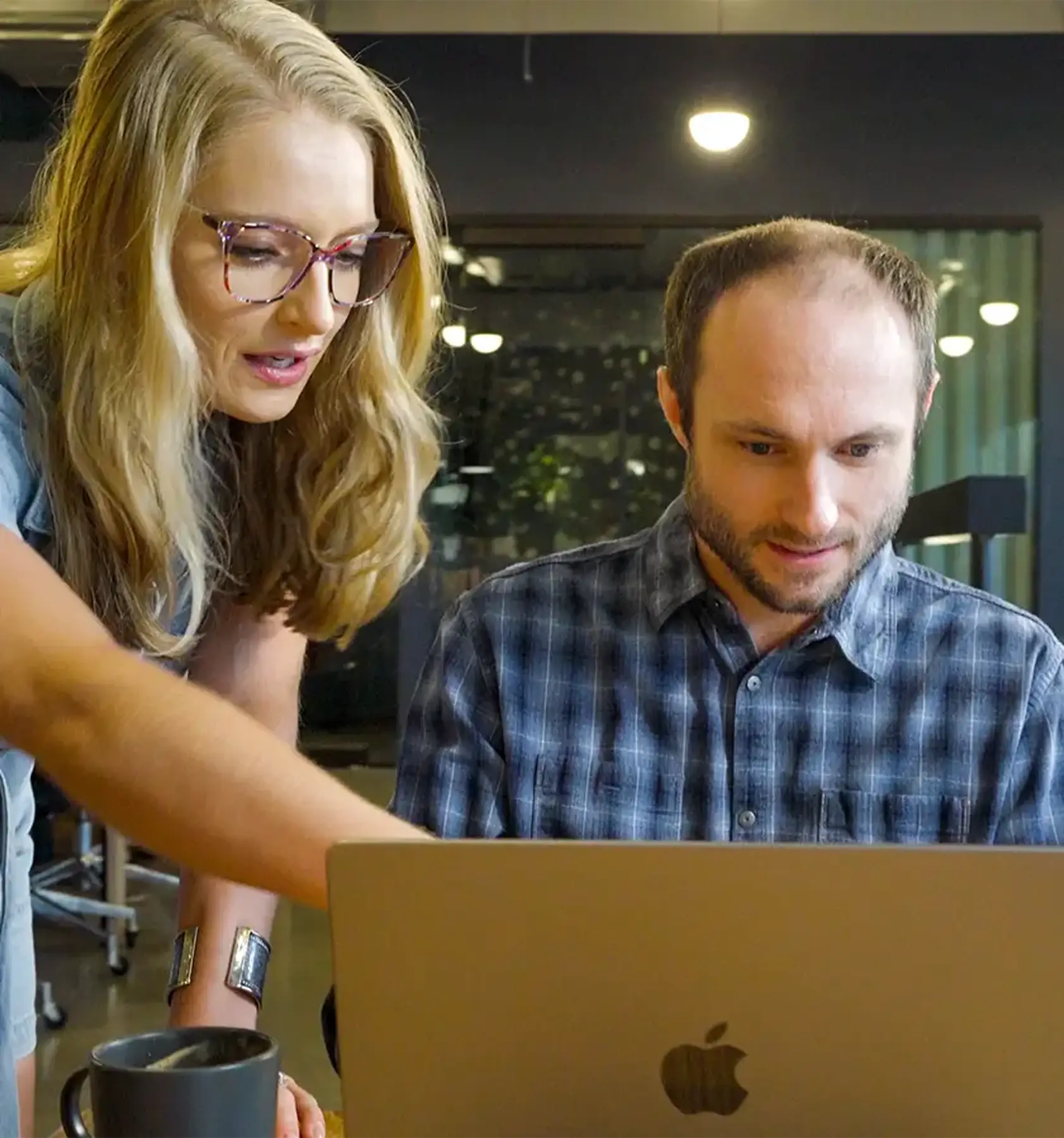 <p>Two coworkers collaborating at a desk, with a woman pointing at a laptop screen while a man looks on attentively in a modern office setting.</p>