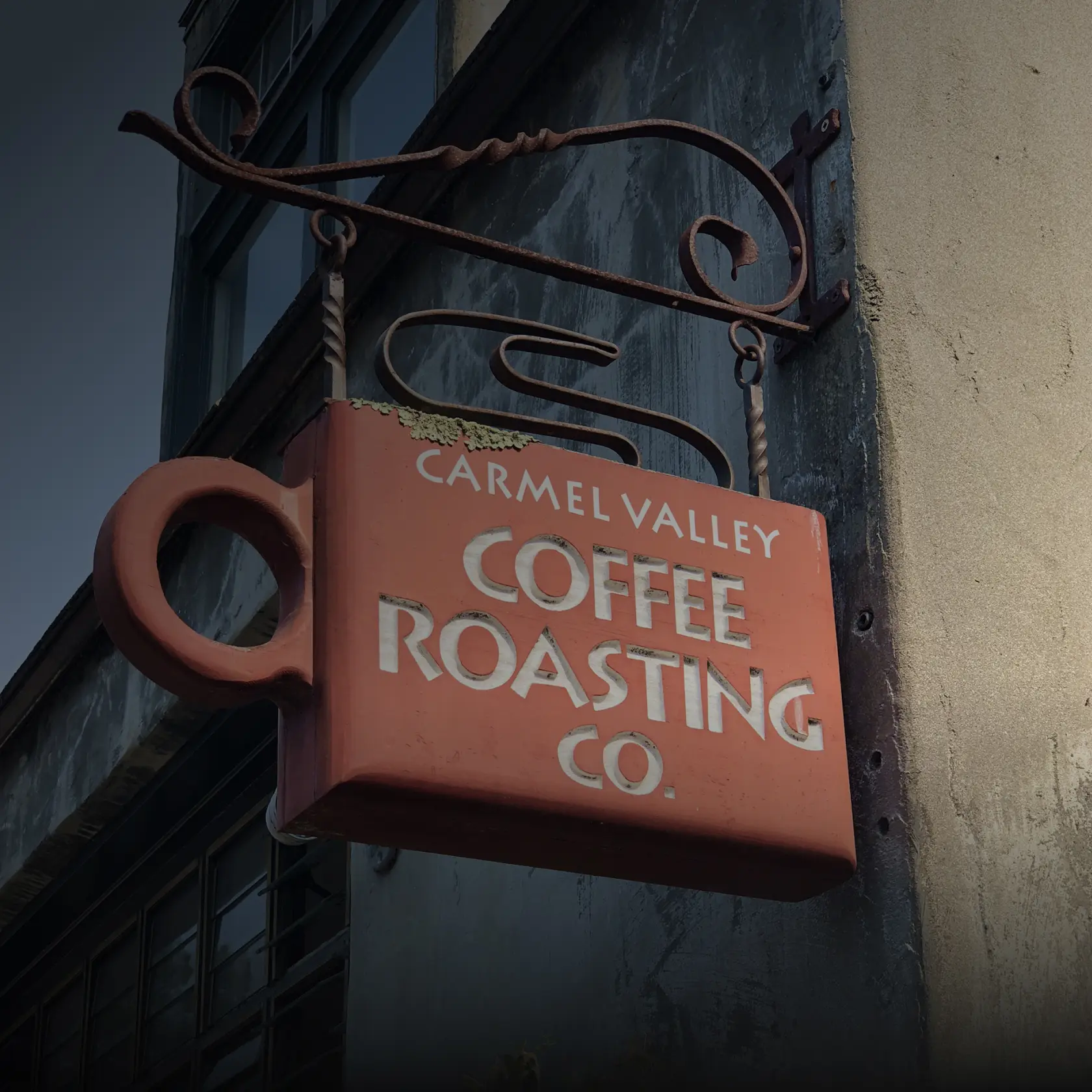 Exterior Carmel Valley Coffee Roasting Co. sign shaped like a coffee cup hanging from a building facade