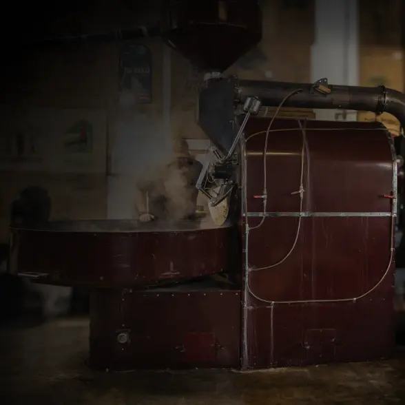 Large coffee roasting machine at Carmel Valley Coffee Roasting Co., with steam rising during the roasting process and a team member working behind the equipment.