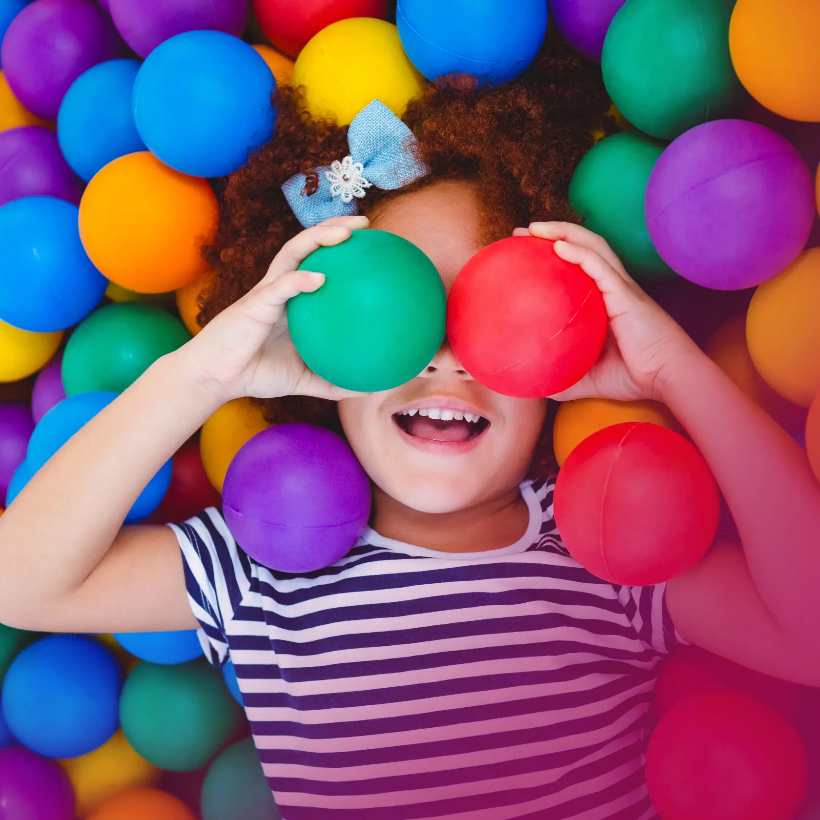 Smiling child holding colorful balls while playing in a bright ball pit.